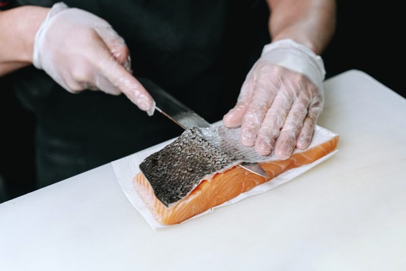 Gloved hands skinning a salmon fillet on a cutting board