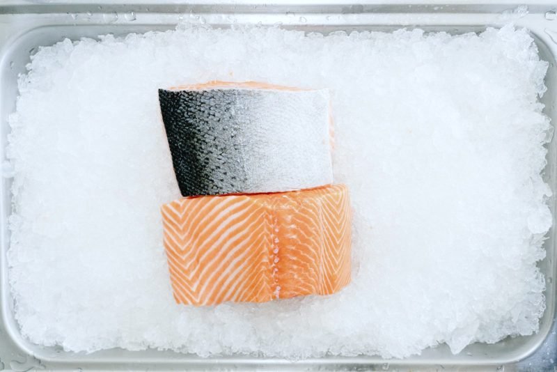 Salmon portions resting on ice in a steel tray